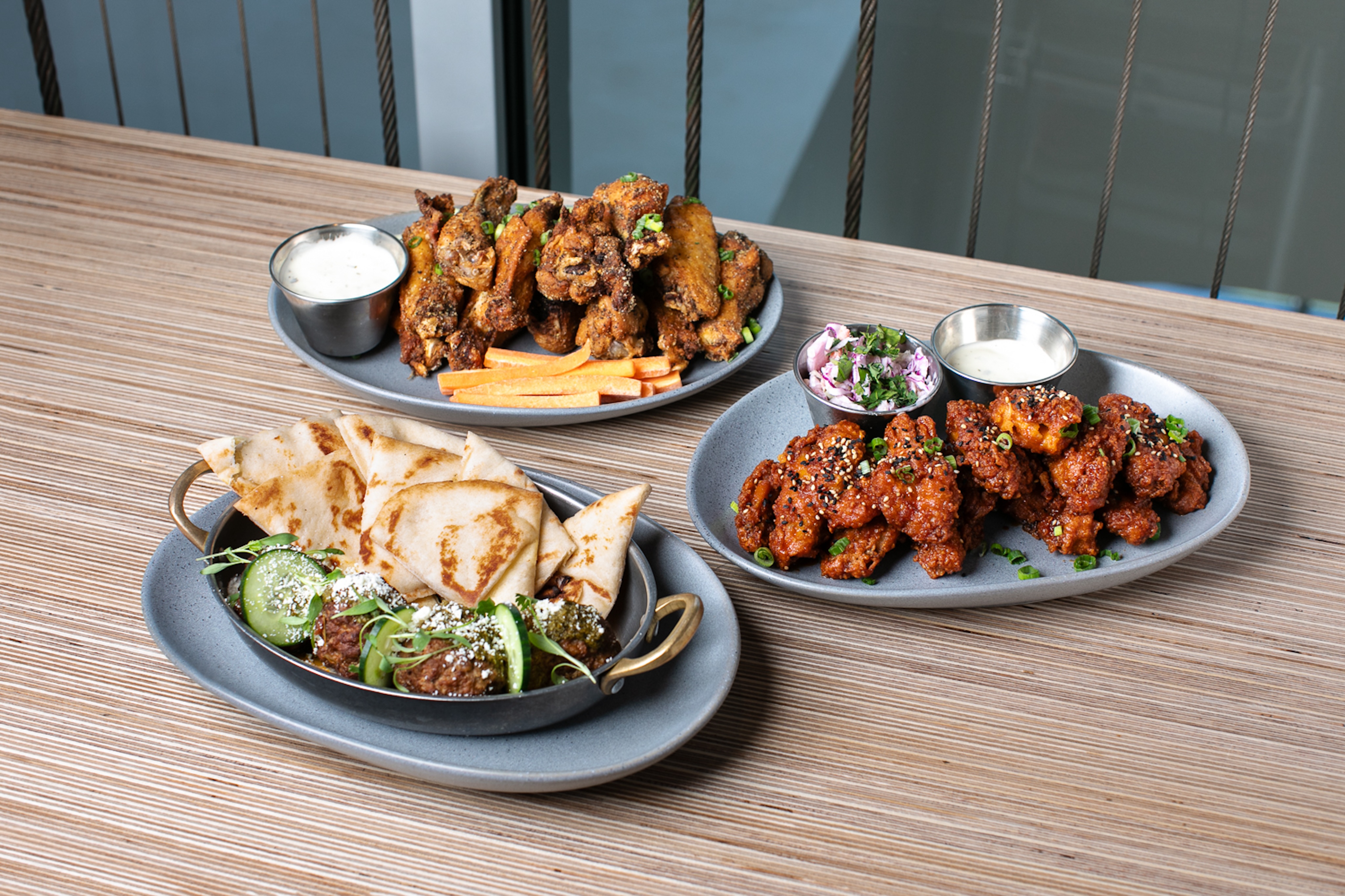 Three dishes on a table: grilled meat with pita and greens from Nest on Four, Instagram-worthy fried chicken wings with dip, and spicy cauliflower bites with HometeamBLeak's signature sauce.