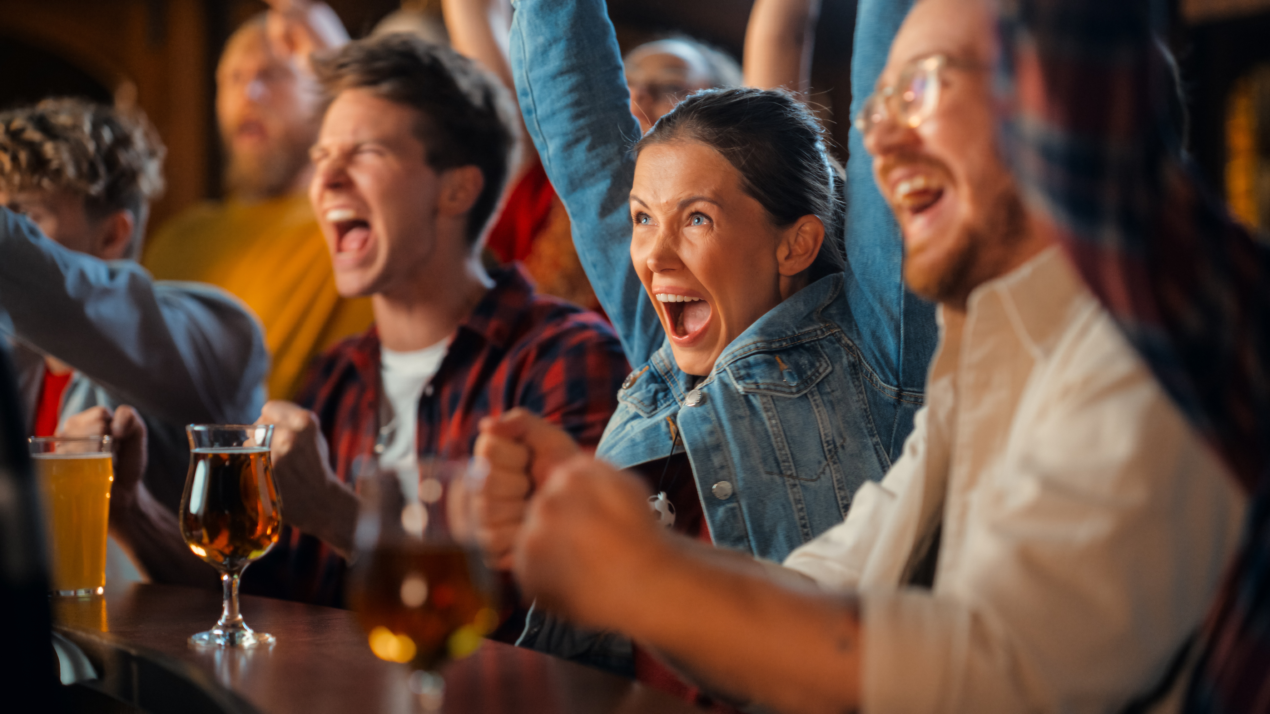 A group of people at The Away End bar enthusiastically cheering for Atlanta United while watching a screen, with drinks on the counter.