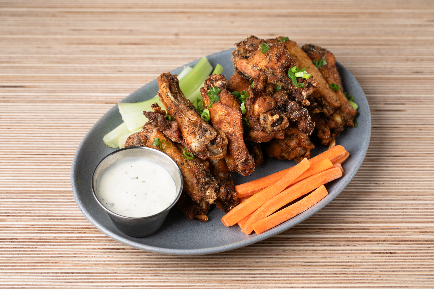 A plate of fried chicken wings, reminiscent of a vibrant art exhibition, is garnished with green onions, celery, and carrot sticks, served alongside a side of dipping sauce.