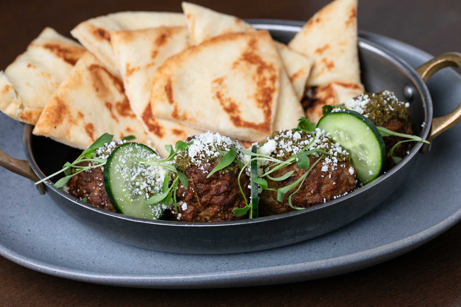 A dish of falafel garnished with cucumber slices and herbs, topped with cheese, served with pieces of pita bread on the side, presented like a masterpiece ready for a food gallery.