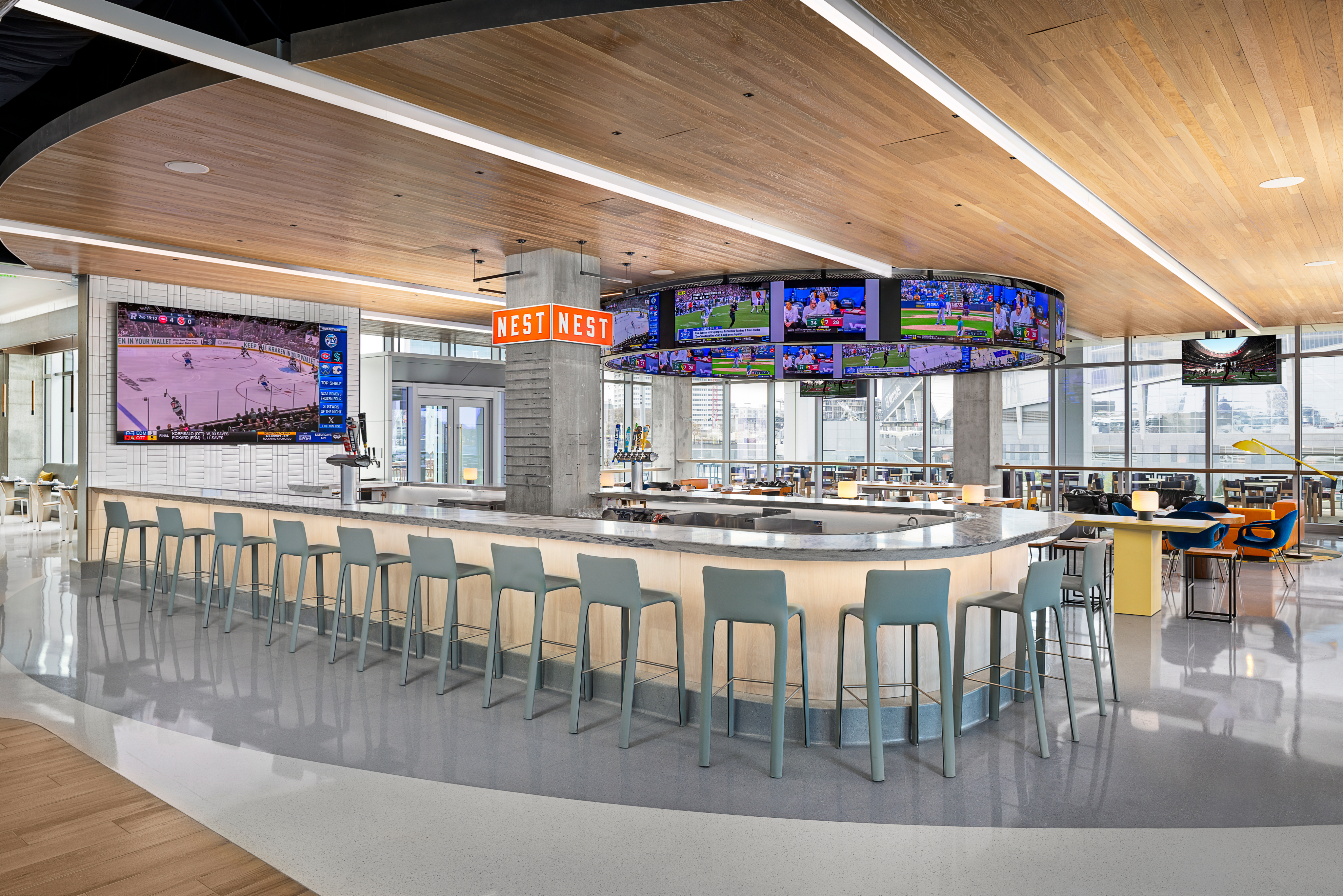 Modern sports bar with a circular counter, high stools, and multiple flat-screen TVs displaying various sports. The wood-paneled ceiling adds warmth and style, making it the ultimate home page for fans seeking a lively atmosphere.